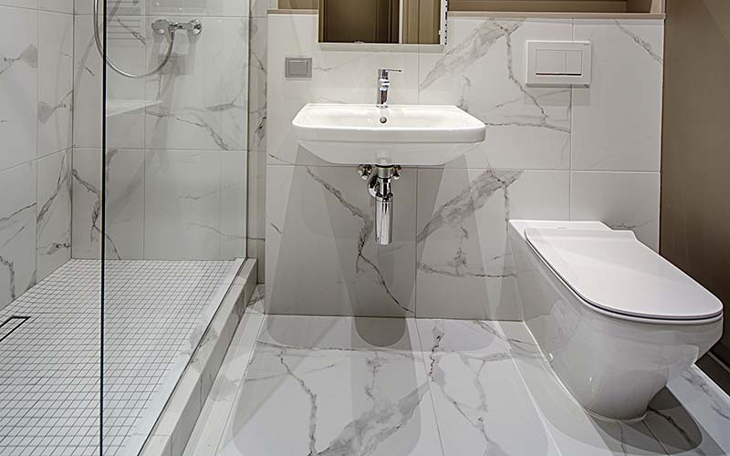 Bany de marbre amb plat de dutxa d'obra, mampara, pica i WC.